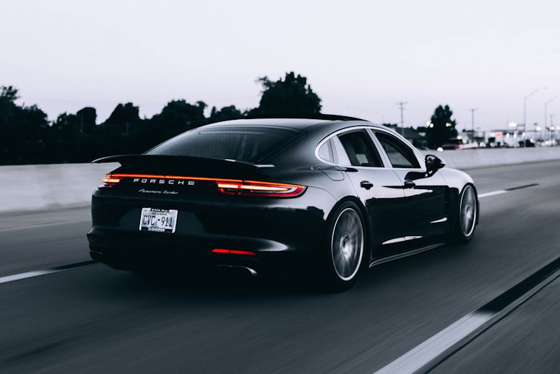 A car parked beside an open road stretching toward distant hills.